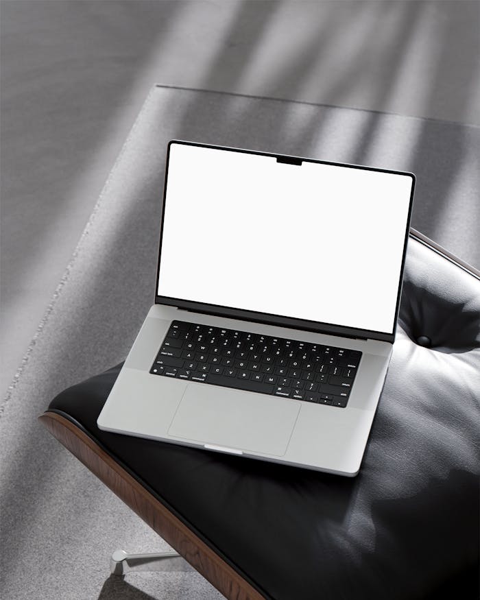 Sleek laptop with a blank screen on a contemporary chair, bathed in sunlight shadows.